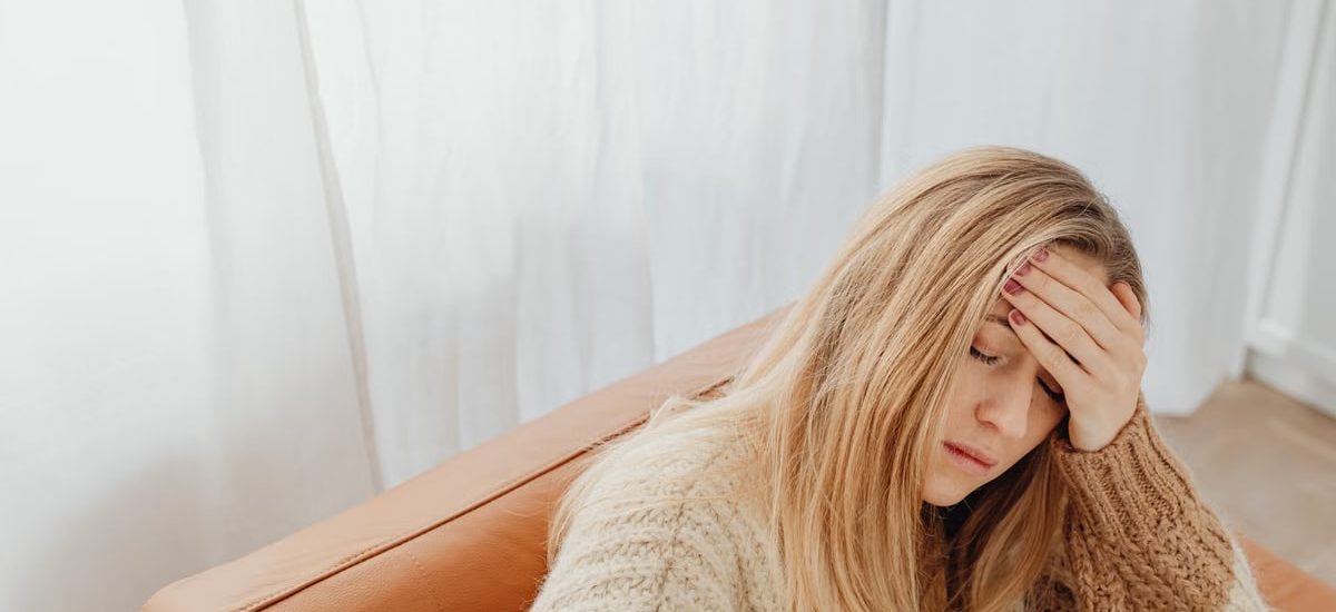 A woman in a knitted sweater sits with a headache on a cozy sofa indoors.