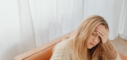 A woman in a knitted sweater sits with a headache on a cozy sofa indoors.