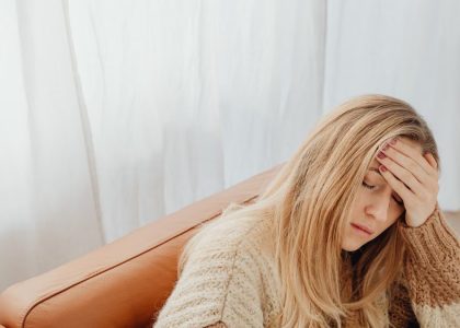 A woman in a knitted sweater sits with a headache on a cozy sofa indoors.